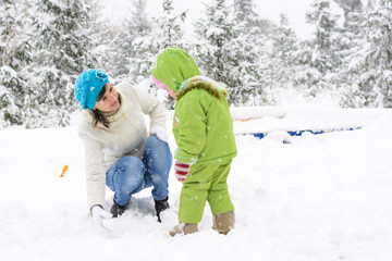 Little baby and mother are playing with first snow