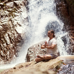 Fototapeta na wymiar a man sits near the mountains with a beautiful waterfall