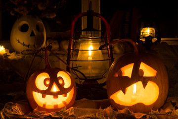 Photo composition from two pumpkins on Halloween. Mad and scared pumpkins stand against an old window, leaves and candles.
