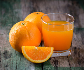 Orange juice glass and fresh oranges on wood