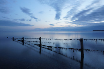 Obraz premium blue sky after sunset at the beach with fence in the water