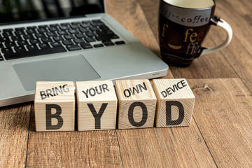 Bring Your Own Device (BYOD) written on a wooden cube in front of a laptop