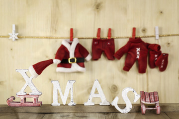 Rote Nikolauskleidung auf der Wäscheleine mit weißen Buchstaben XMAS vor Holzwand