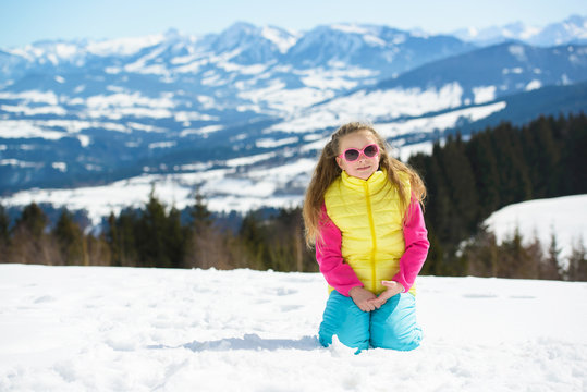 Smiling little girl in sunglasses  in winter mountains on a sunny day