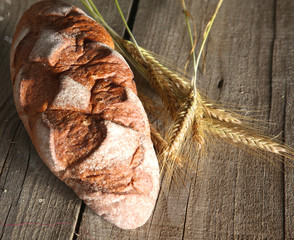 rustic crusty bread and wheat ears on a dark wooden table