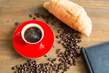 Coffee cup and beans, with croissant, notepad  on wooden background