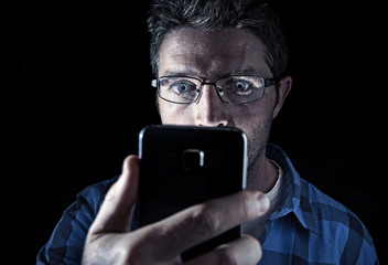 close up portrait of young man looking intensively to mobile phone screen with blue eyes wide open...
