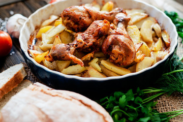 baked chicken legs in garlic marinade with baked potatoes , sauce , tomatoes , bread and herbs on wooden background