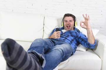 20s or 30s man alone lying on couch listening to music with mobile phone and headphones