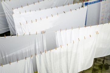 side view of freshly washed sunlit sheets drying outside on a rope