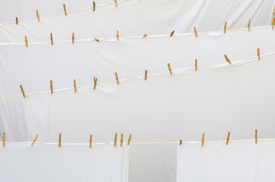 background of many freshly washed white bed sheet layers drying on ropes with wooden pins