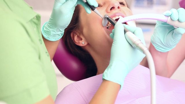 Female dentist and her assistent starting to work on teeth of woman sitting in a dental chair / camera moving left