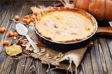 American homemade pumpkin pie , pumpkin seeds and autumn leaves on a wooden background
