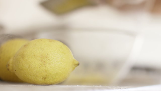 4K Lemon foreground close up as a baker zests a lemon in the background, in slow motion 