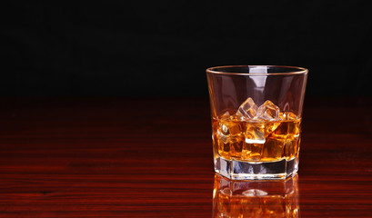 Glass of alcohol scotch whiskey with ice cube on wooden table an