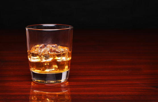 Glass of alcohol scotch whiskey with ice cube on wooden table an