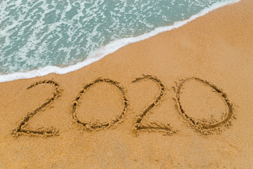 2020 inscription written on sandy beach with wave approaching