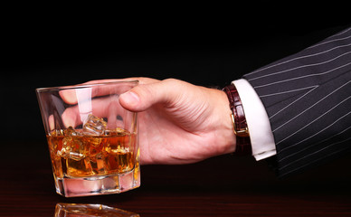 rich and success business man holding in hand glass of alcohol scotch whiskey with ice cube on wooden table and black background