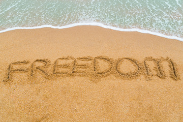 FREEDOM inscription written on sandy beach with wave approaching