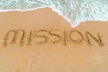 MISSION inscription written on sandy beach with wave approaching