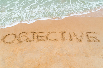 OBJECTIVE inscription written on sandy beach with wave approachi
