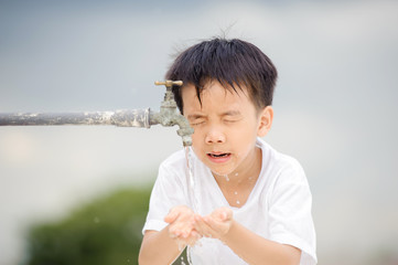 Young Asian boy use water from old faucet to wash his face and hair on grey cloud on the sky before rain.