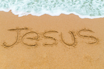 JESUS inscription written on sandy beach with wave approaching