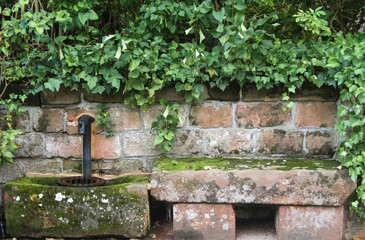 Old stone bench and water tap covered with moss