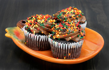 Three chocolate fall decorated cupcakes on a pumpkin plate.
