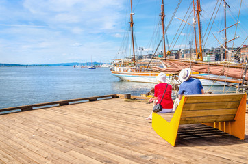 Elderly couple on bench of pier, Oslo, Norway - obrazy, fototapety, plakaty