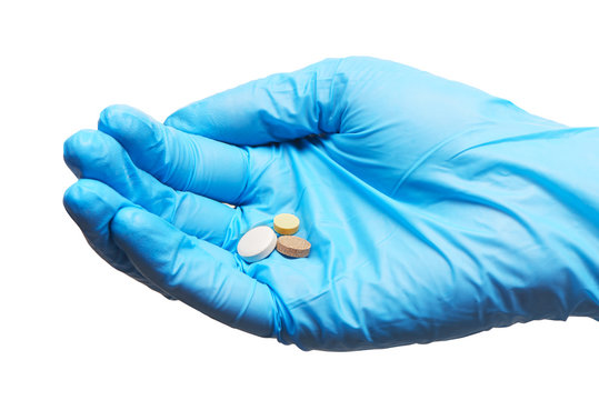 Close up of three round white, yellow and brown tablets on female doctor's hand in blue sterilized surgical glove against white background
