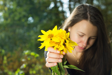Naklejka premium Beauty girl holding bunch of yellow flowers and relaxing in autu