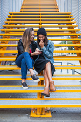 A pair of young and beautiful female friends are sitting on the steps of a staircase...
