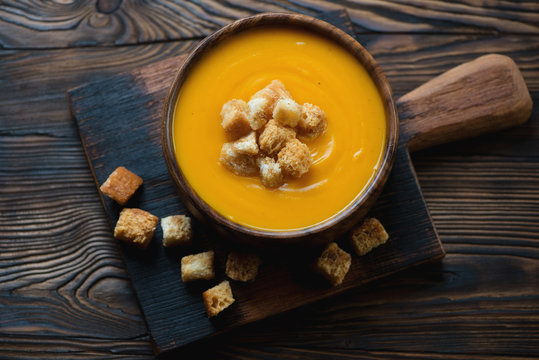 Wooden rustic cutting board with a bowl of pumpkin cream-soup