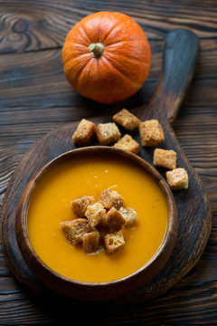 Bowl with pumpkin cream-soup on a rustic wooden cutting board