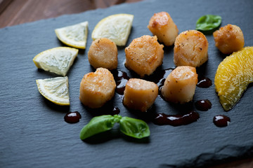 Fried sea scallops with orange fillet, lemon slices and sauce