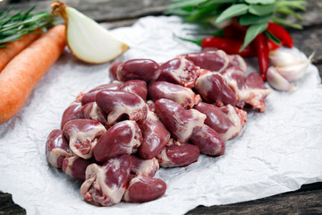 Raw Duck hearts on crumpled paper, decorated with vegetables. on old wooden table