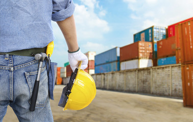 Engineer holding a yellow helmet for the safety of workers on the background stock port with containers.