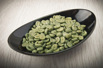 Black bowl with green coffee beans on the wood