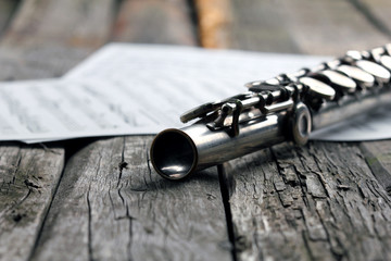Old silver flute and music notes on rusty table