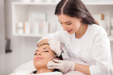 Fototapeta na wymiar Attractive expert beautician is injecting female face