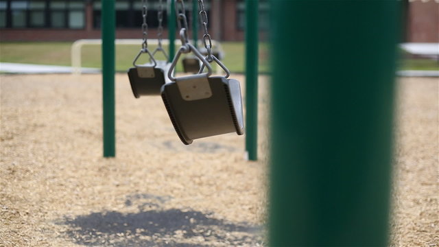 Swing Fast School Background Selective Focus. a long shot with shallow depth of field on a row of swings with a school in the background. closest swing sways quickly back and forth

