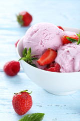 Ice cream in bowl with strawberries on blue wooden background