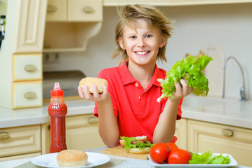 smiling boy holding a hamburger bun and salad in the kitchen