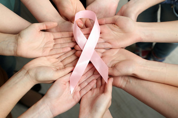 Group of female hands with pink ribbon as breast cancer awareness symbol, closeup