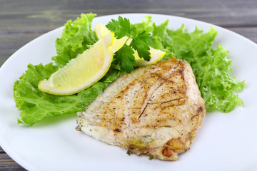 Dish of fish fillet with lettuce and lemon on table close up
