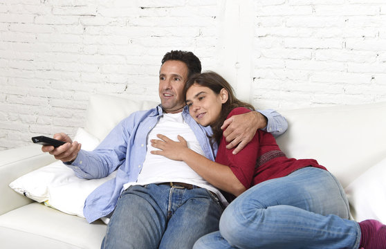 couple in love cuddling on home couch relaxing watching movie on television with man holding remote control