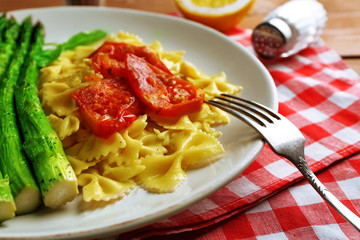 Roasted asparagus and tasty pasta with vegetables on plate on wooden table background