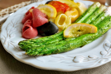 Roasted asparagus and tasty colorful pasta with vegetables on plate on wooden table background