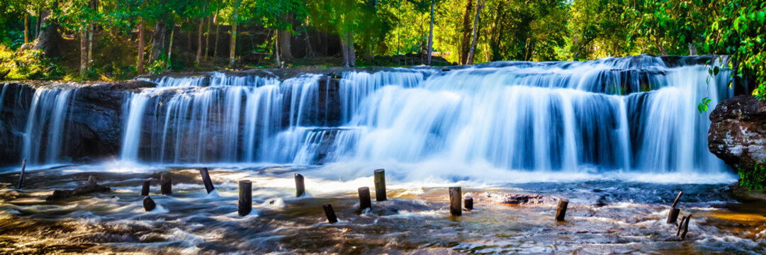 Fototapeta Fototapeta Wodospad z niebieską wodą wśród słonecznych lasów XXL